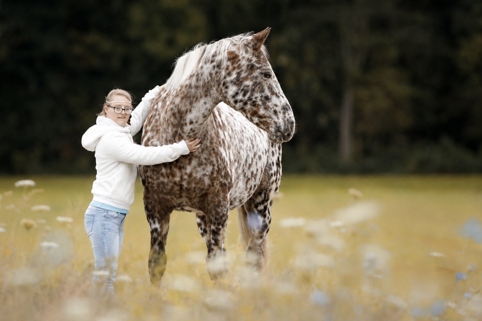 Kind umarmt einen Knabstrupper auf der Weide beim Therapiereiten in Andwil TG